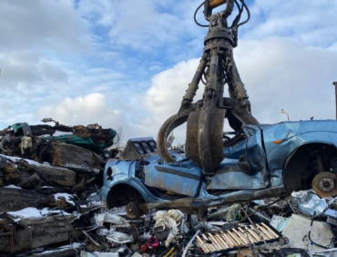 A scrap metal handling grab picking up a scrap vehicle from a pile of scrap metal.